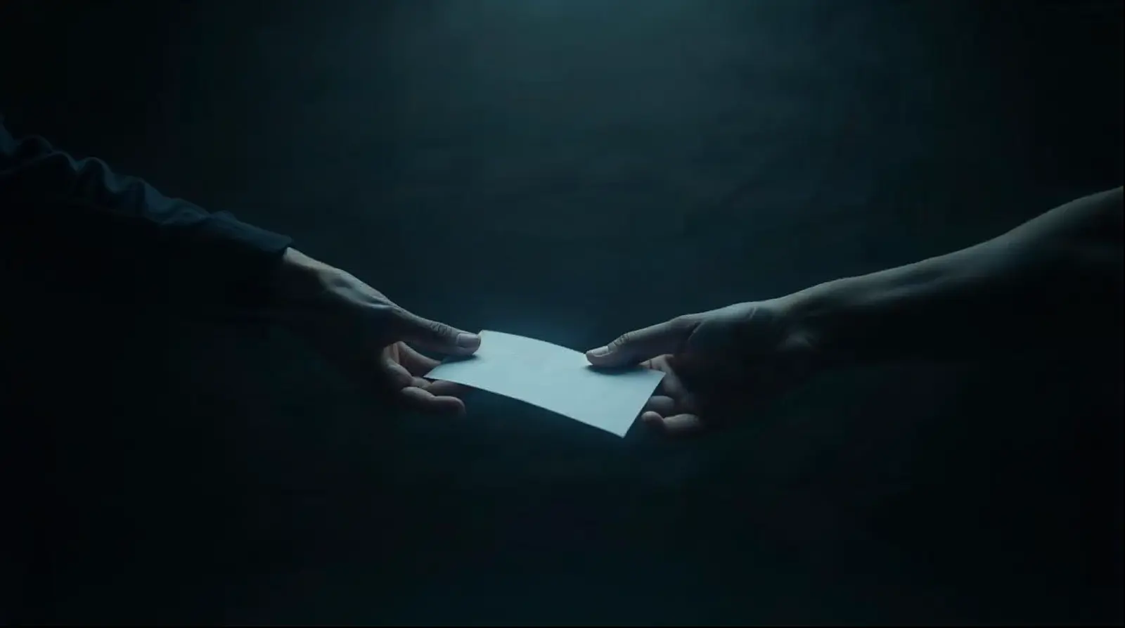 Close-up: a folded note passes from one hand to another, in an empty space. Nobody else.